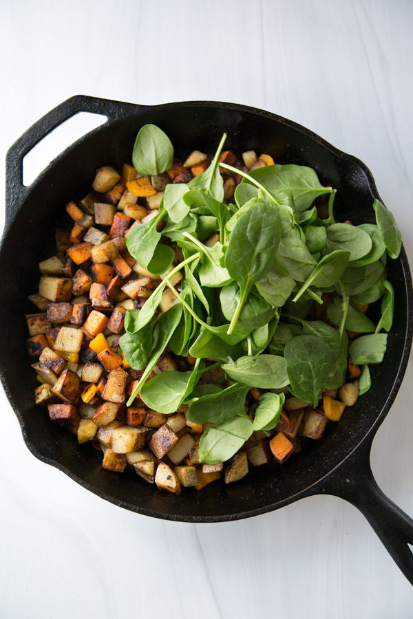 skillet with low fodmap breakfast hash and fresh spinach leaves on top