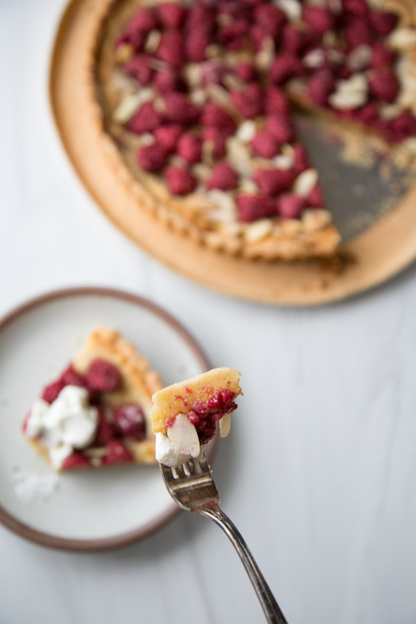 Fork holding piece of raspberry and almond frangipan tart on a plate