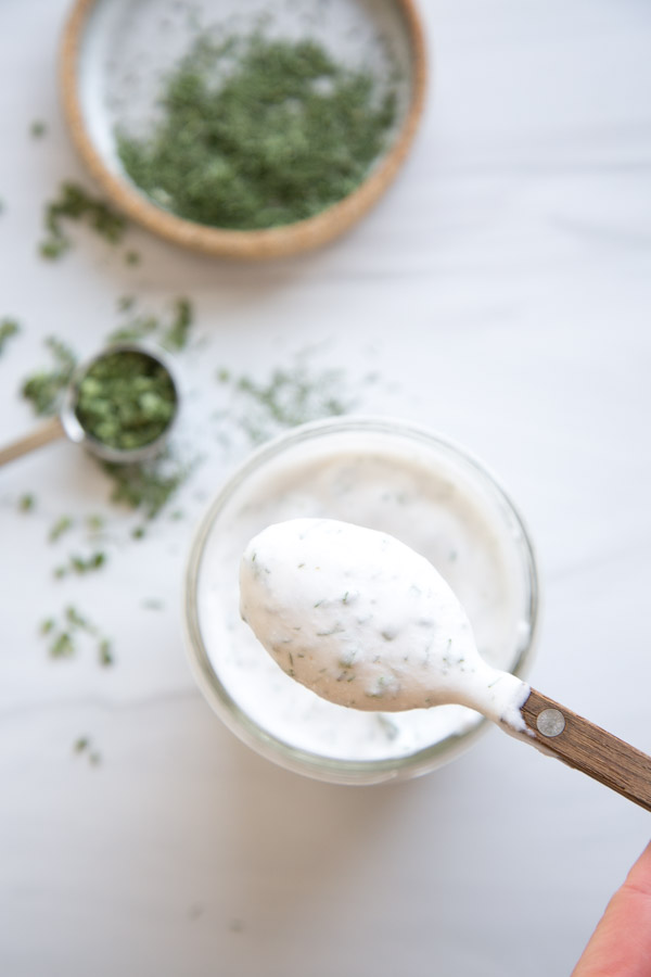 Hand holding a spoon of gluten free ranch dressing with dried chives next to it