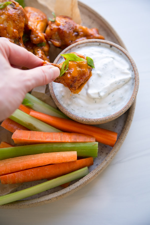 Hand dipping Gluten-free buffalo wings in dairy-free ranch dressing