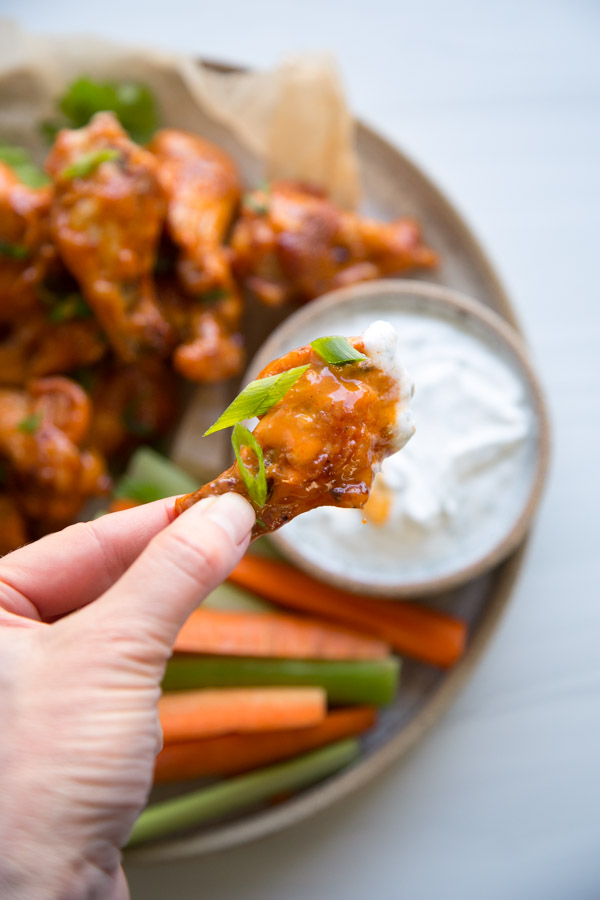 hand holding Gluten-free chicken wing dipped in dairy-free ranch 