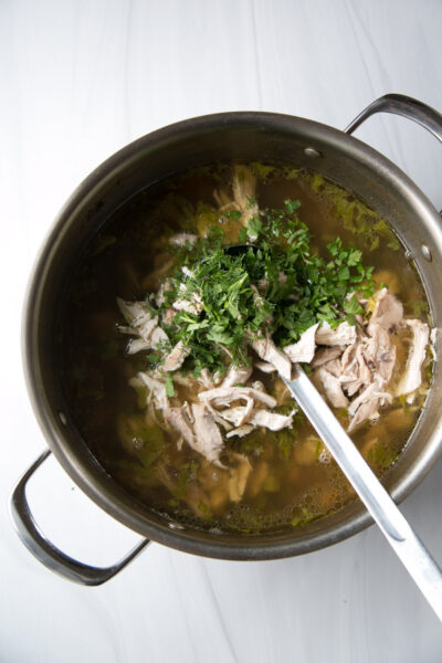 Jewish chicken noodle soup in a pot with shredded chicken thighs and herbs