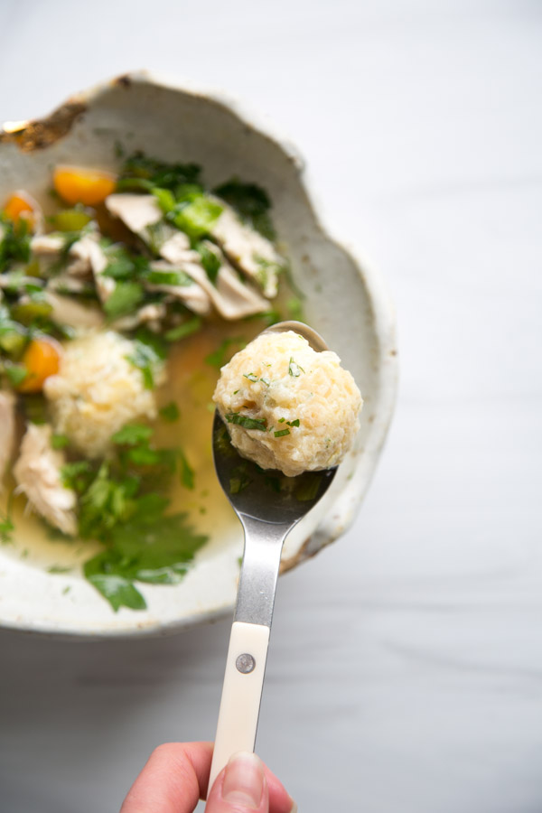 spoon holding gluten-free matzo ball for passover over bowl of jewish chicken soup