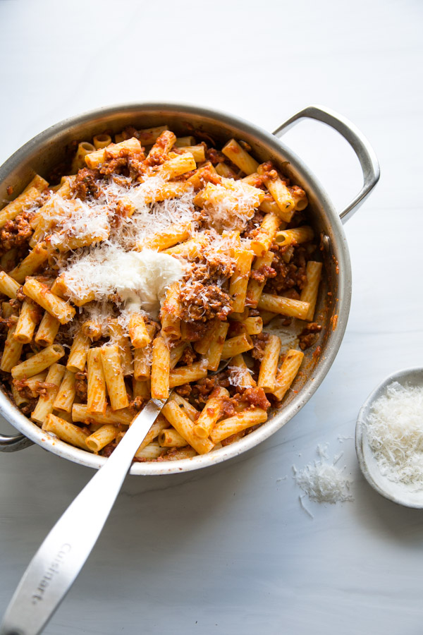 low fodmap pasta bolognese with ground turkey in a saucepan with spoon and parmesan on the side