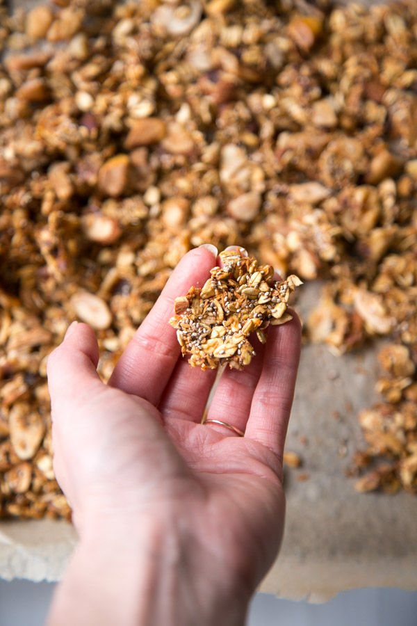 hand holding a cluster of sugarless granola over a sheet pan