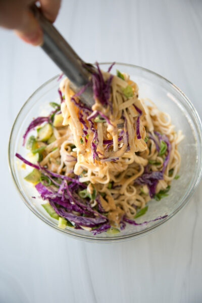 Use tongs to transfer cold sesame noodle salad and Asian dressing to mixing bowl