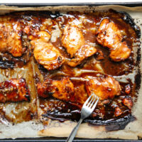 Baked chicken thighs glazed with a dark, sticky sauce on a parchment-lined baking sheet, with a silver fork resting on the tray.