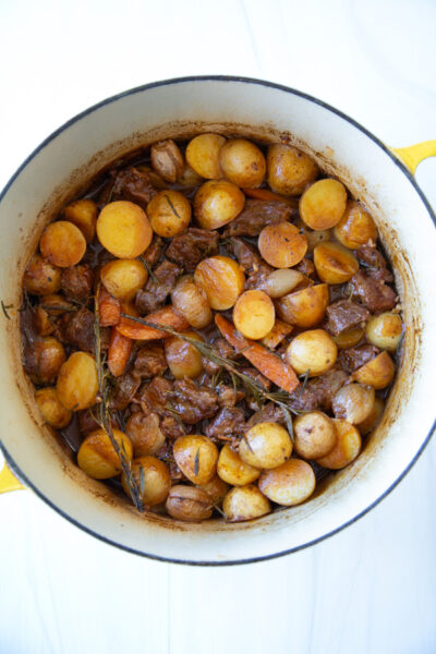Beef stew with potatoes, carrots, and sprigs of rosemary in a yellow enameled cast iron pot.