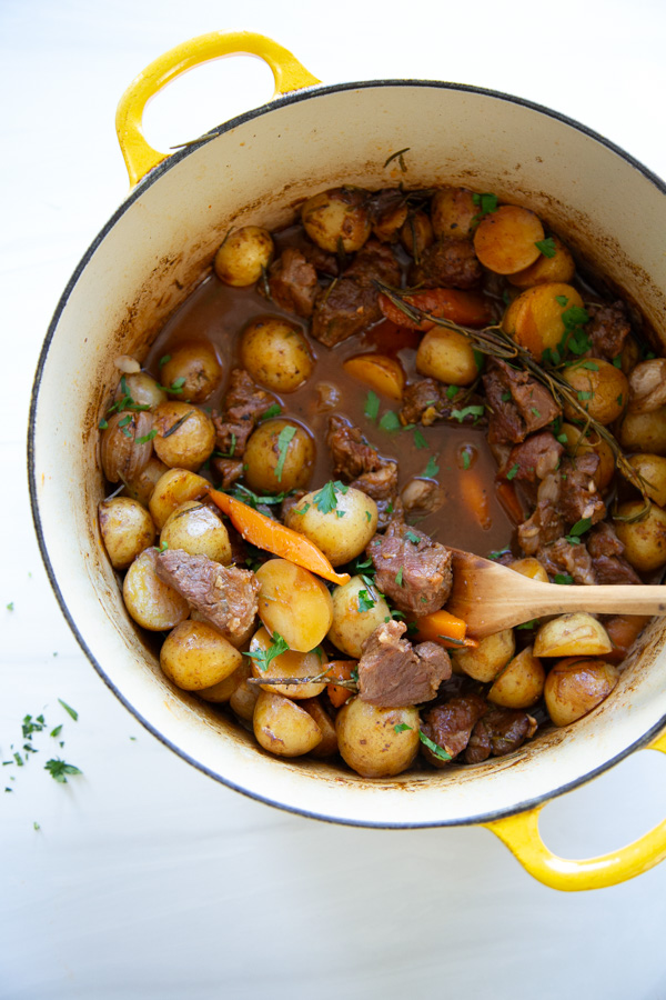 A yellow enameled cast iron pot filled with a beef and potato stew, garnished with fresh herbs.